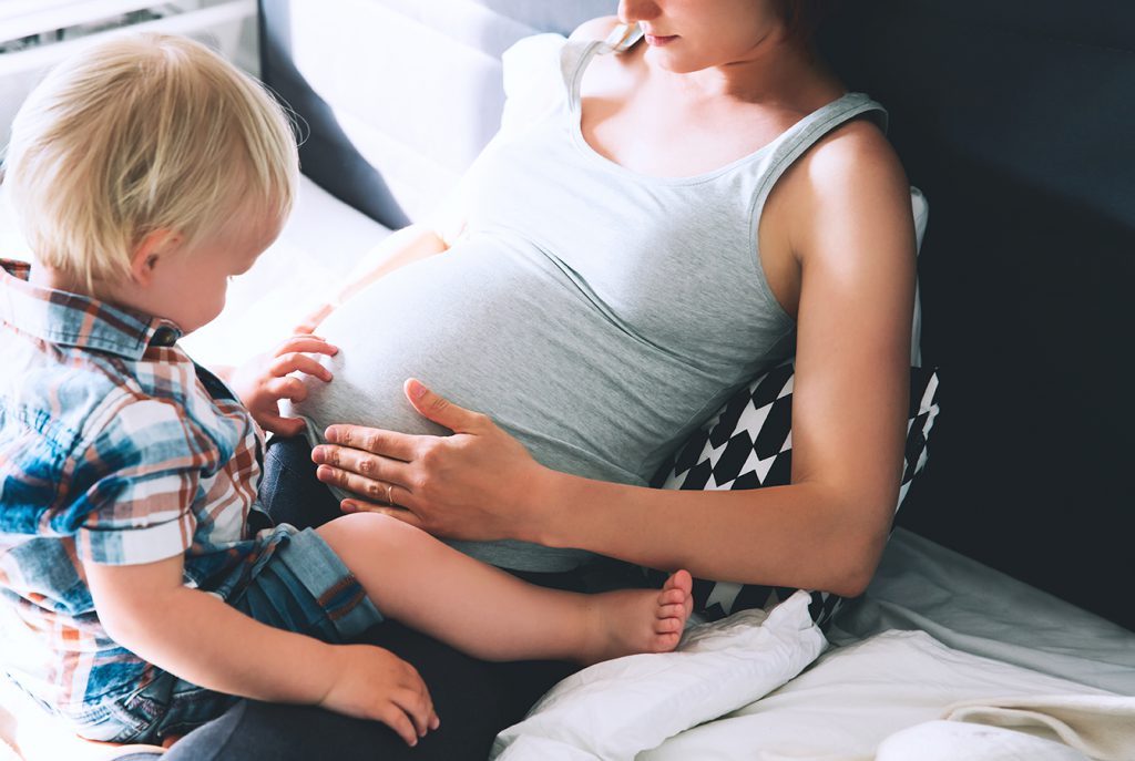 zwangere vrouw zit met haar zoon op bed en maken contact met ongeboren kind